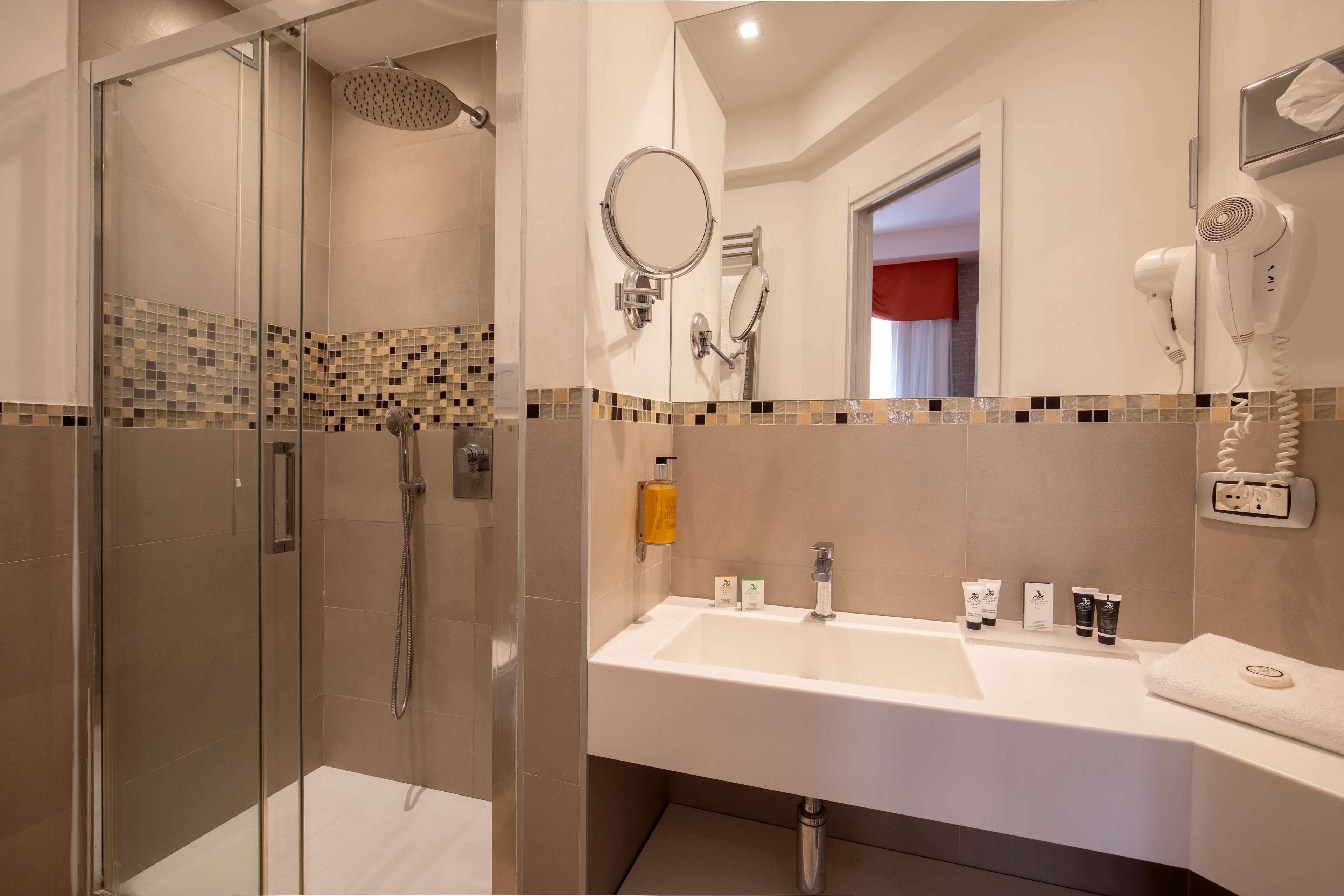 A modern bathroom with a glass-enclosed shower, a white sink with toiletries, and a hairdryer mounted on the wall.