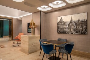 Een moderne eetruimte met een marmeren receptiebalie, blauwe gestoffeerde stoelen en een groot stadsgezichtschilderij aan de muur.