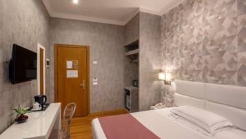 Habitación de hotel con cama, mesita de noche, televisor y una pared con diseño geométrico.