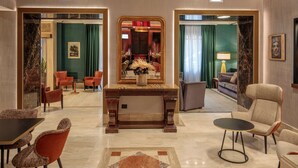 Un vestíbulo de hotel con suelo de mármol, mostrador de recepción, zonas de estar y un espejo que refleja la estancia.