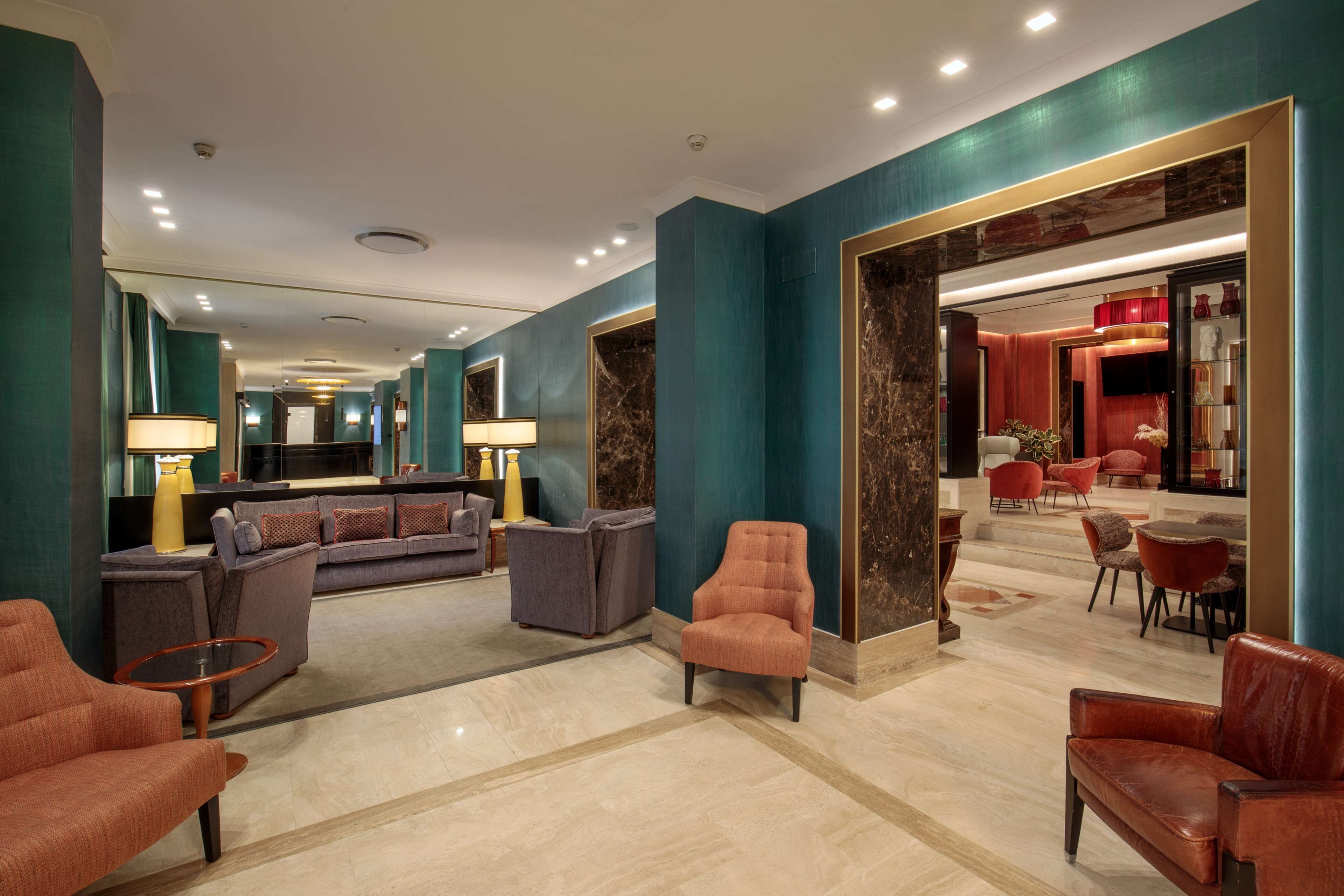 A spacious lobby with a modern design, featuring a seating area with sofas and armchairs, a marble floor, and a large mirror.