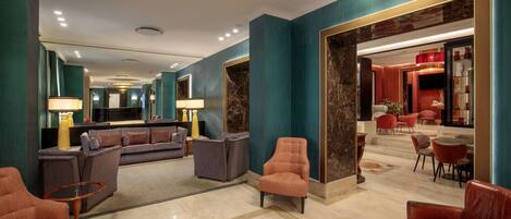A spacious lobby with a modern design, featuring a seating area with sofas and armchairs, a marble floor, and a large mirror.