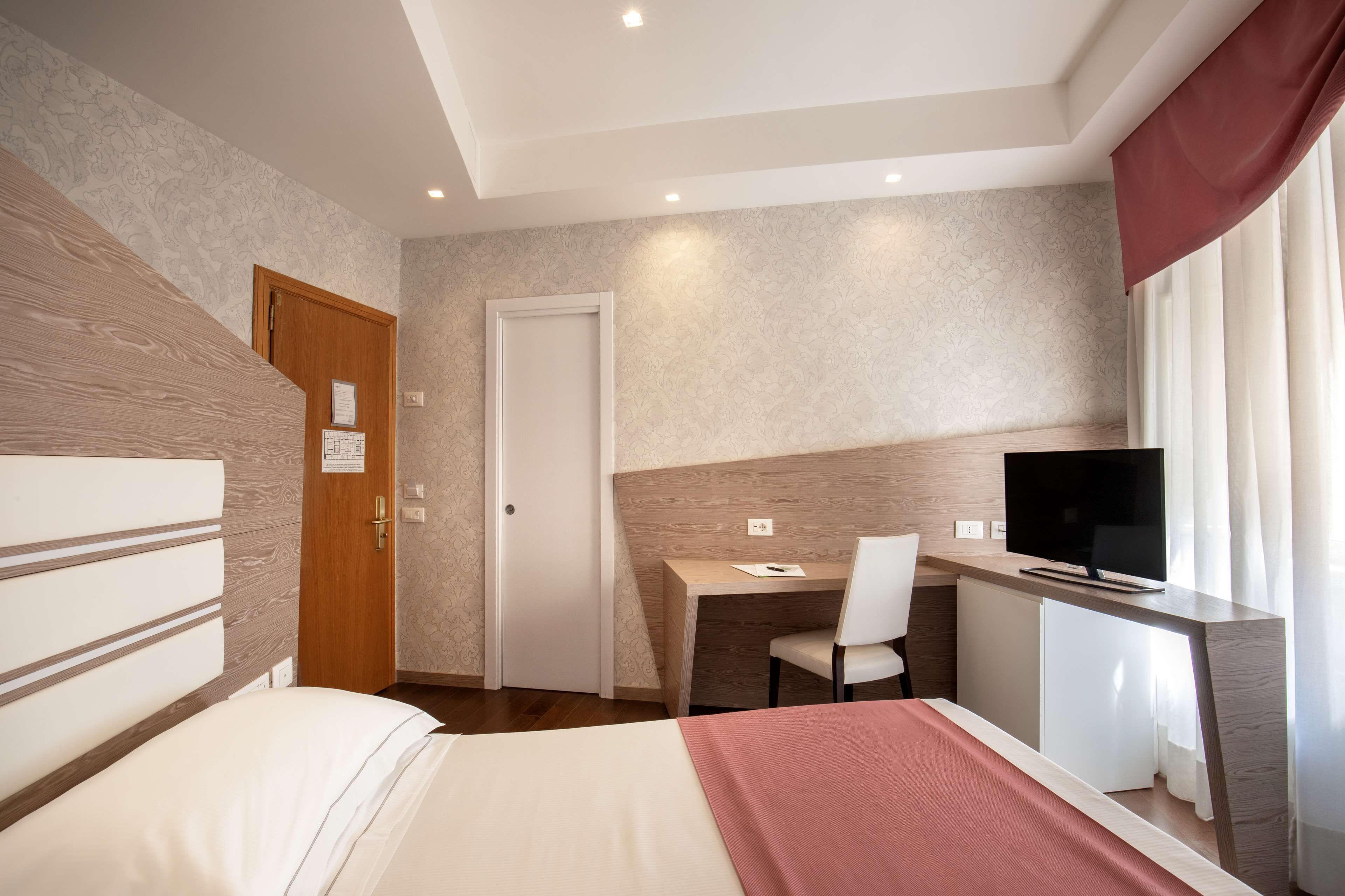 A hotel room with a bed, a desk with a chair, a television, and a door.