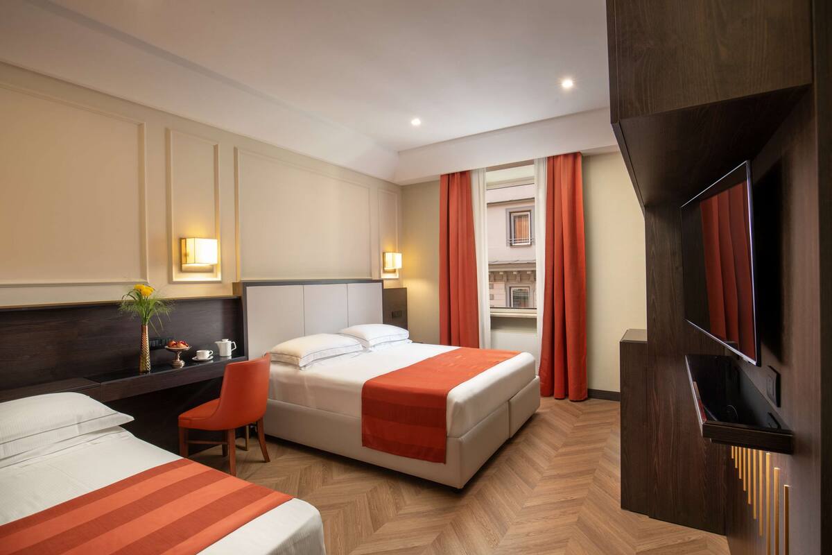 A hotel room with two beds, a desk, a chair, a TV, and a minibar.