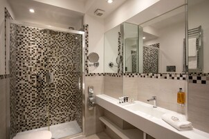 A modern bathroom with a glass-enclosed shower, a large mirror, and a white sink with toiletries.