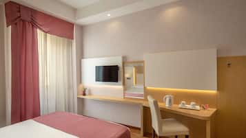 A hotel room with a bed, a desk with a chair, a TV mounted on the wall, and a mirror above the desk.