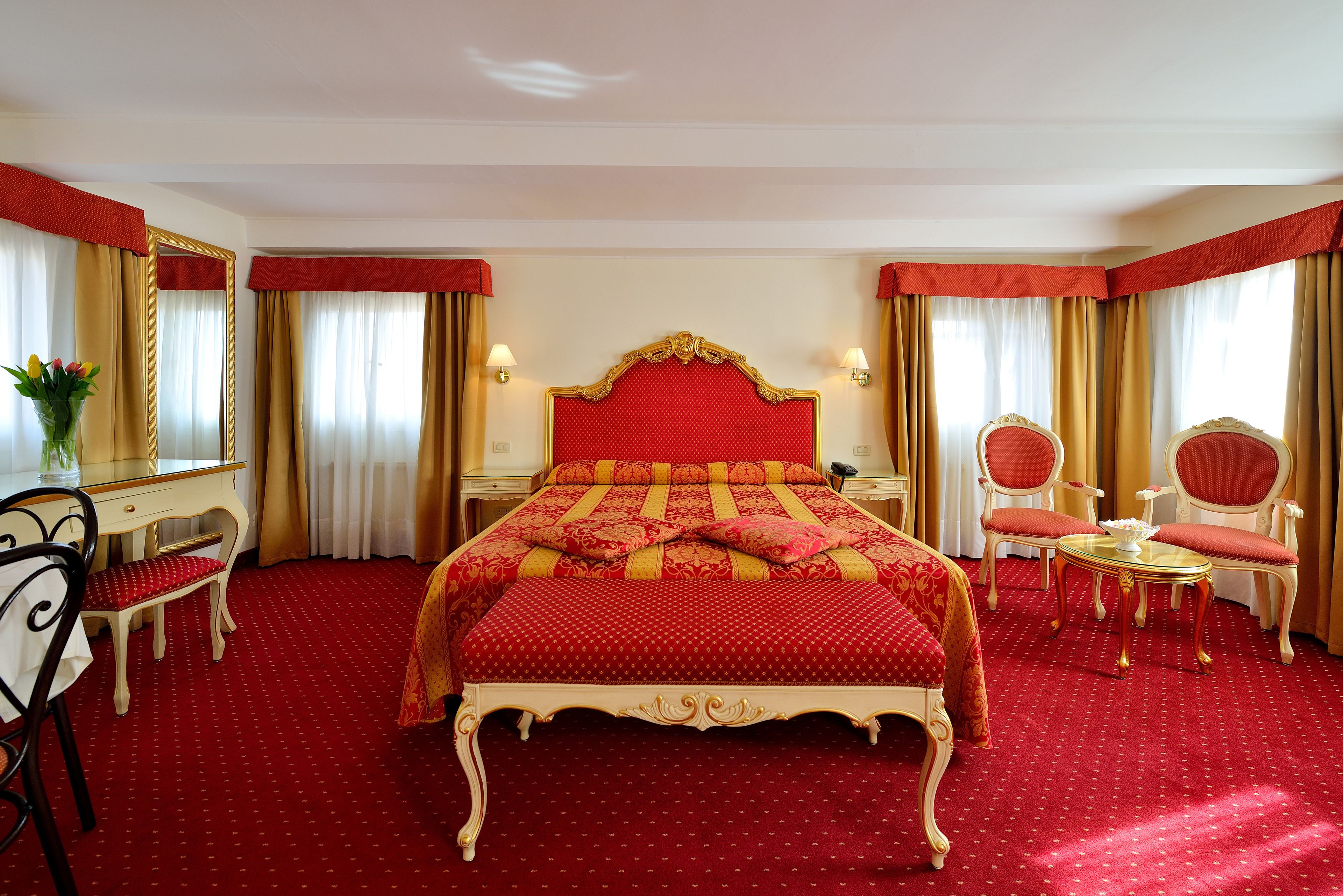 A hotel room with a large bed, two bedside tables, a desk, a chair, and a small table with a mirror.