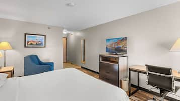 A hotel room with a large bed, a desk, a chair, a TV, and artwork on the walls.