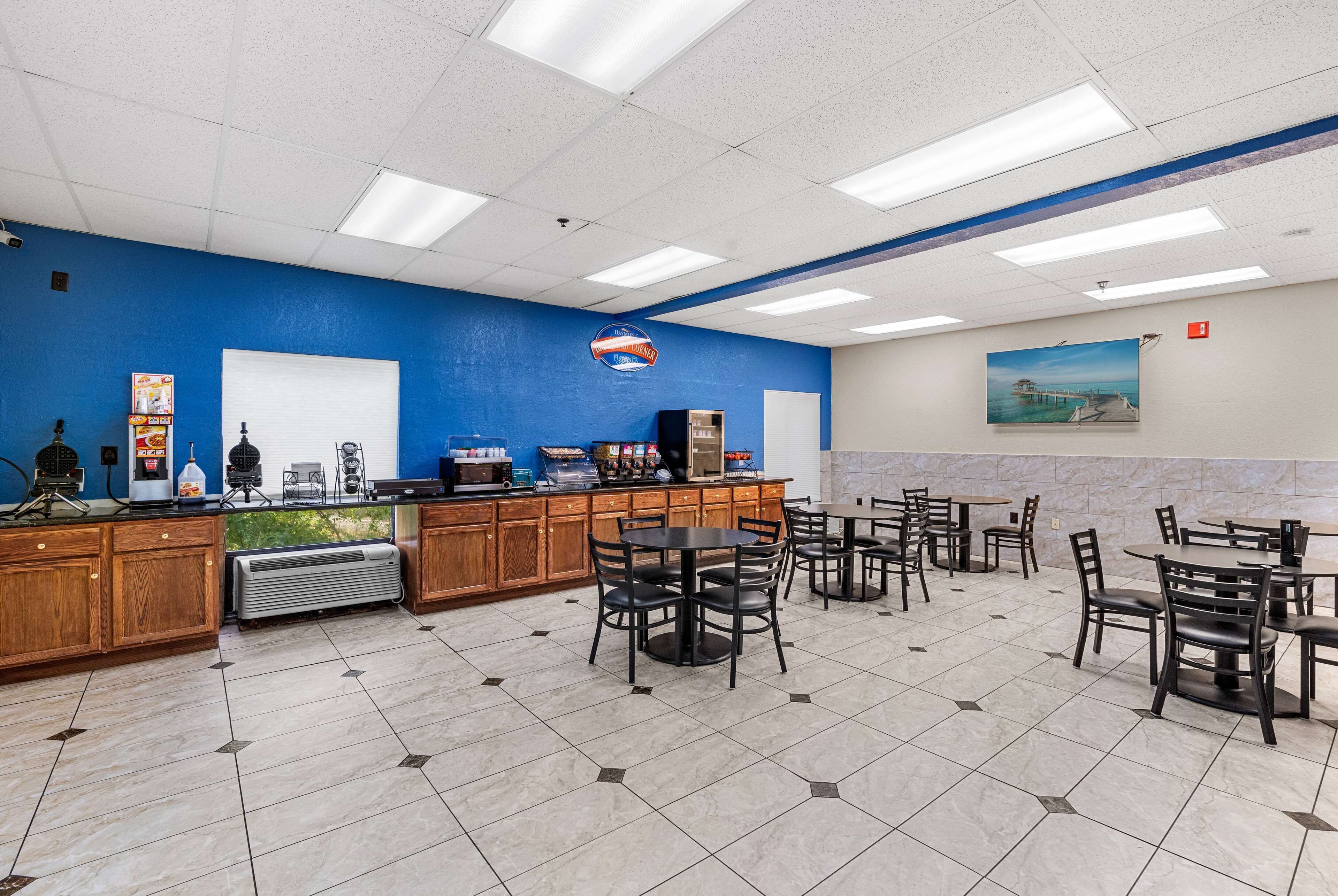 Une cafétéria dotée de nombreuses tables et chaises, d’un coin café et d’une grande fenêtre donnant sur un espace verdoyant.