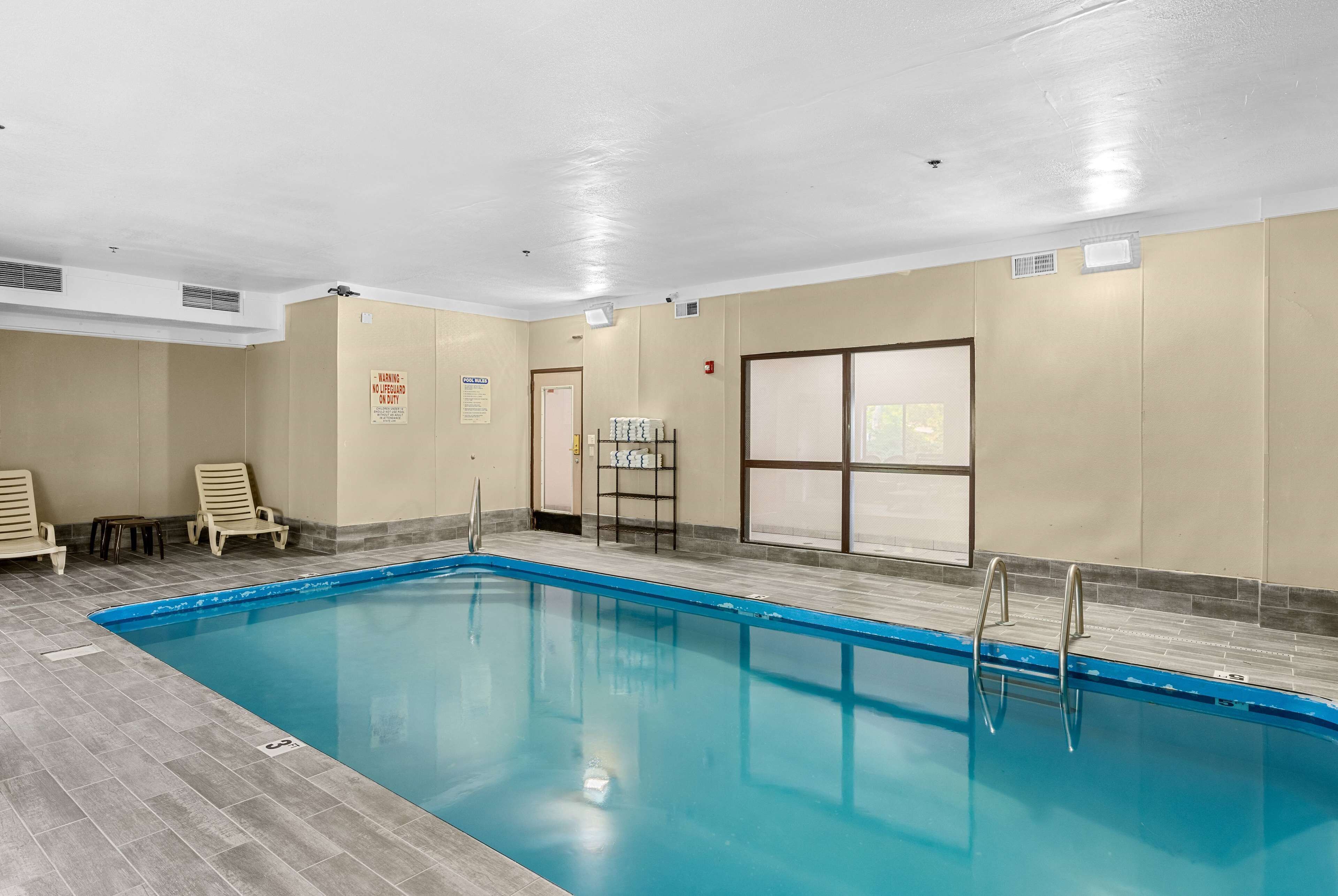 Una piscina interior con suelo de baldosas, algunas sillas de descanso y un calentador de agua en la pared.
