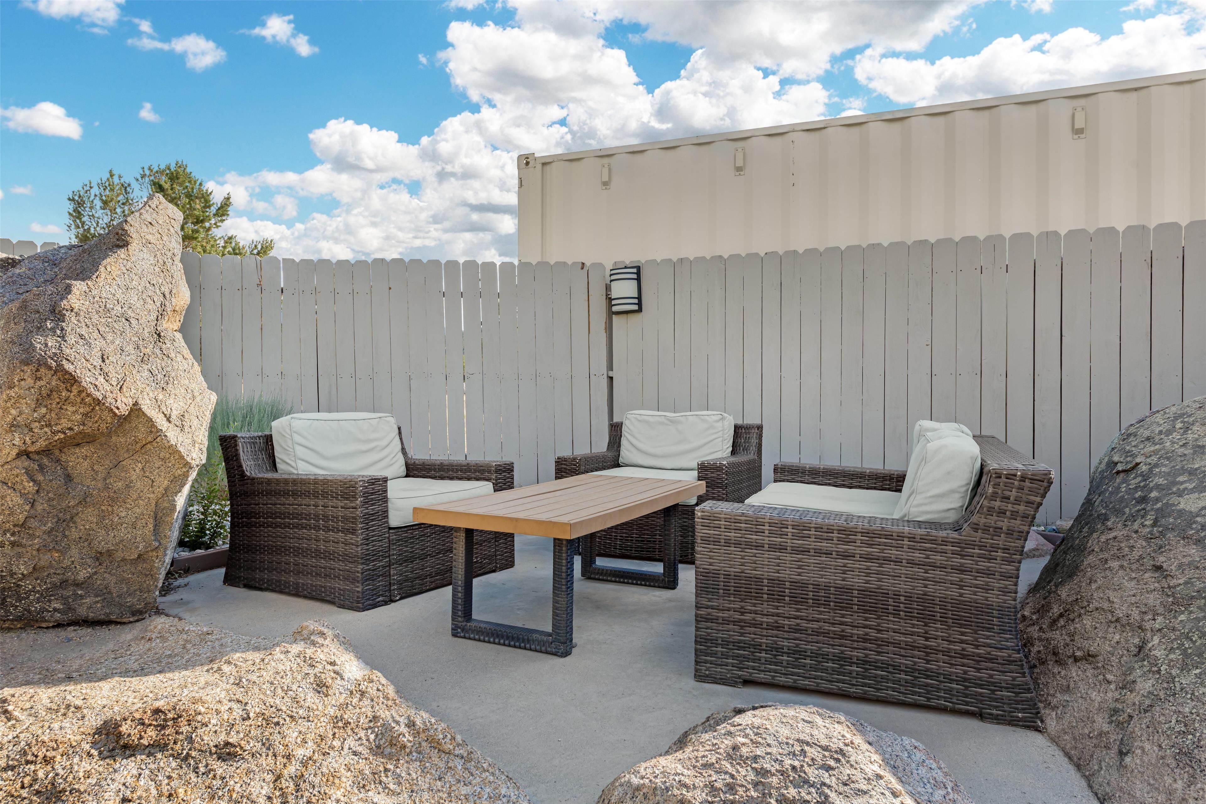 An outdoor patio with wicker furniture, a table, and a white picket fence.
