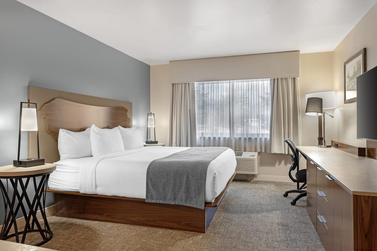 A hotel room with a large bed, bedside tables, a desk, a television, and a window with curtains.