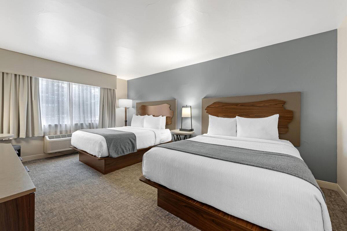 A hotel room with two beds, a desk, and a large window with curtains.