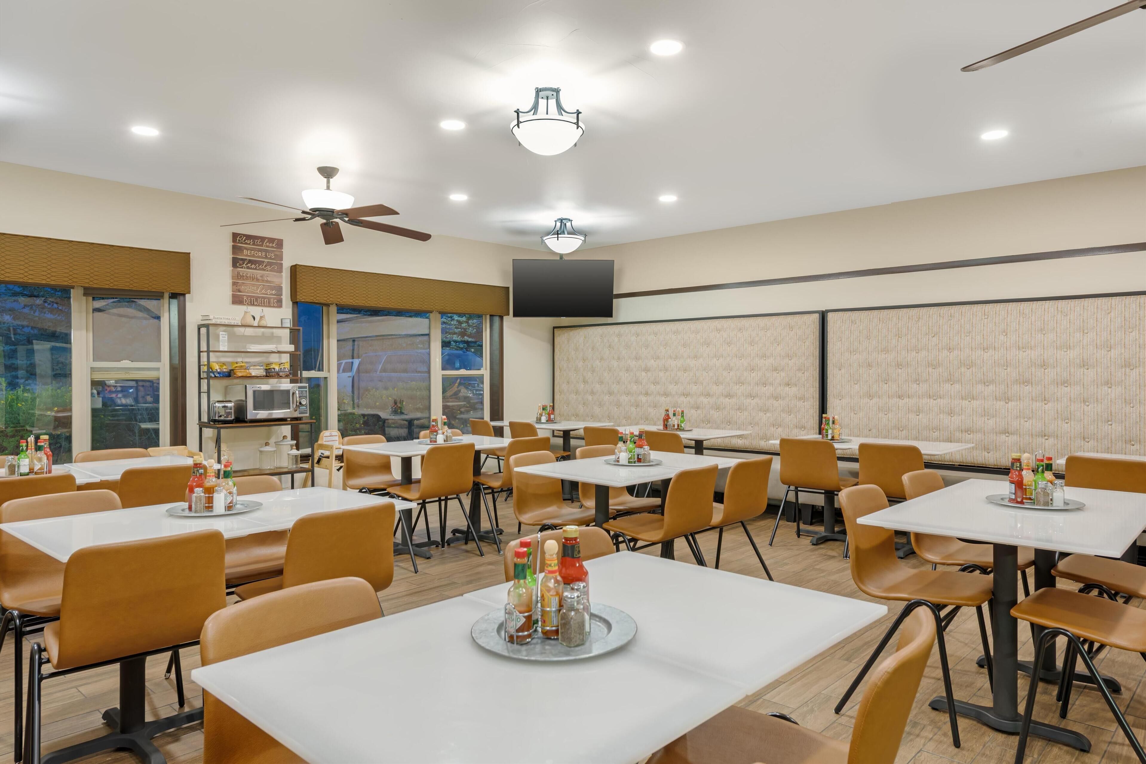 A dining area with multiple tables and chairs, ceiling fans, and a large window providing a view of the outdoors.