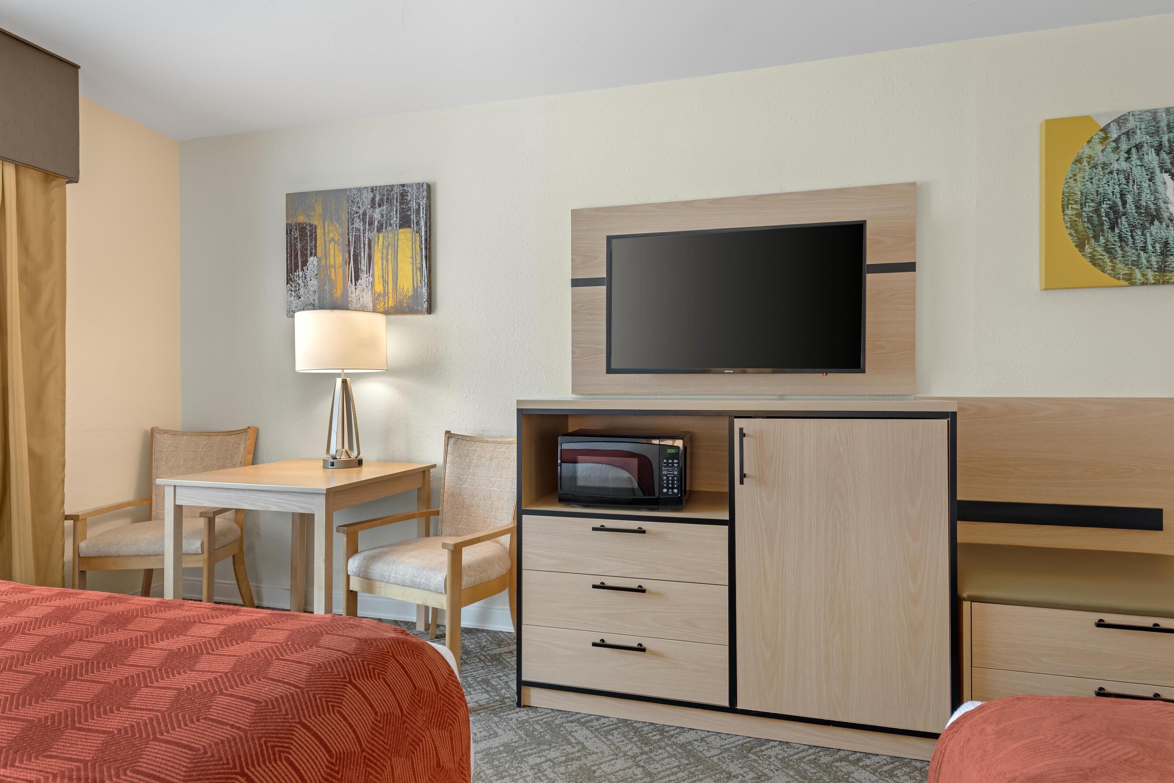 Una habitación de hotel con una cama, un escritorio con lámpara, un televisor, un microondas y un armario.