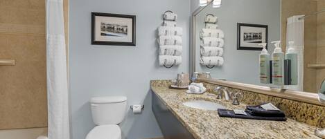 Un baño moderno con inodoro, lavamanos y ducha. Hay toallas colgadas en ganchos y un espejo sobre el lavamanos.