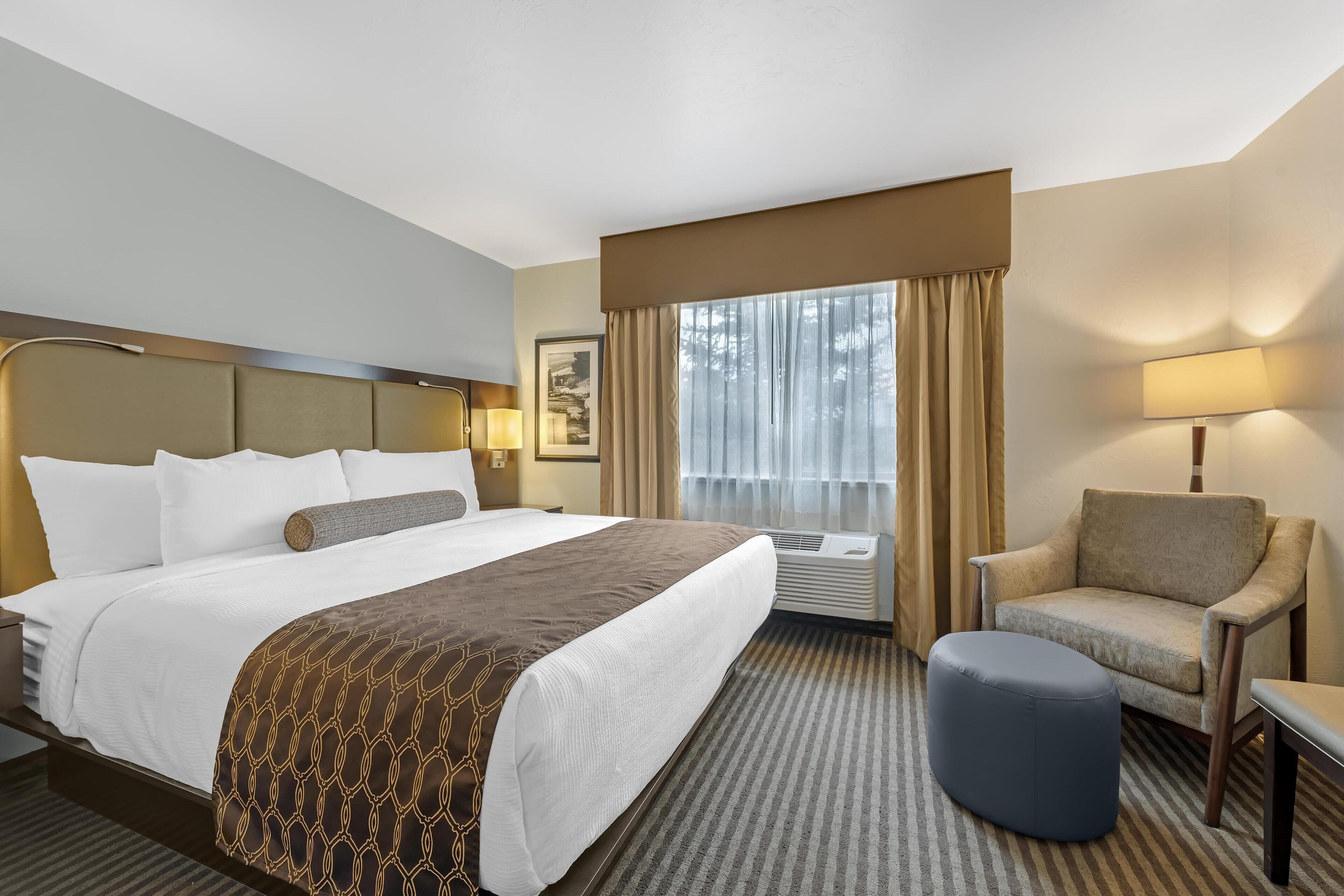 Una habitación de hotel con una cama grande, una silla, una mesita y un ventanal con cortinas.
