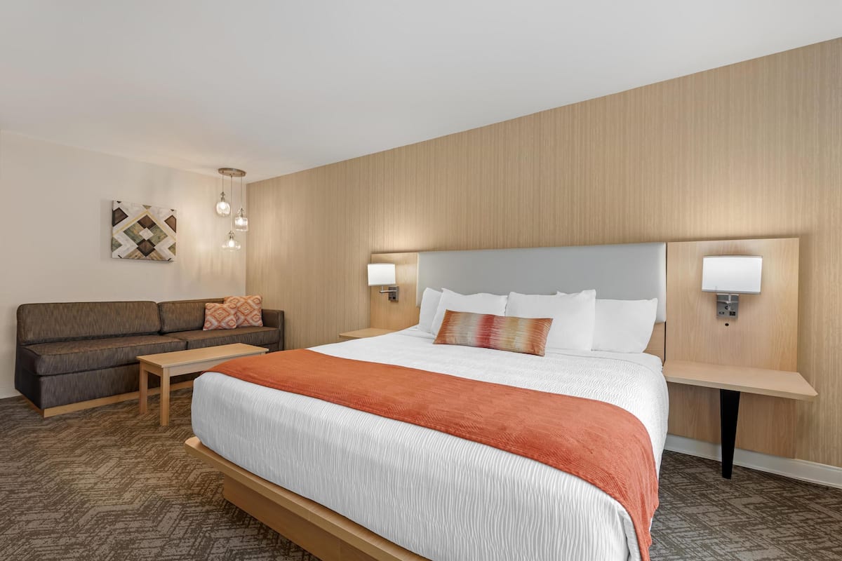 A hotel room with a large bed, a sofa, a nightstand, and a wall-mounted lamp.