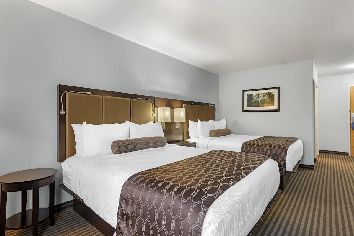 A hotel room with two beds, a round table, and a painting on the wall.