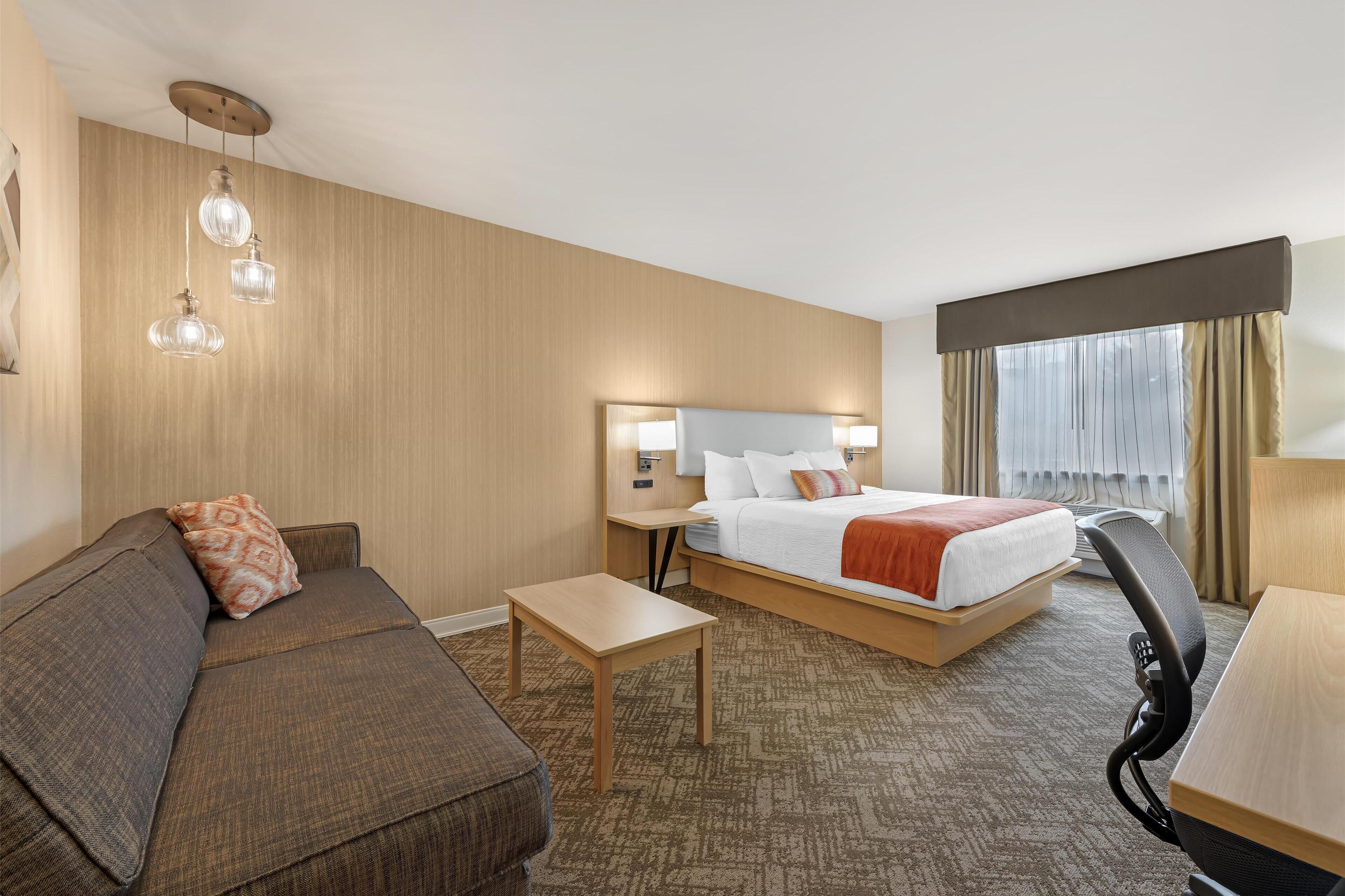 A hotel room with a bed, a sofa, a desk, and a small table.
