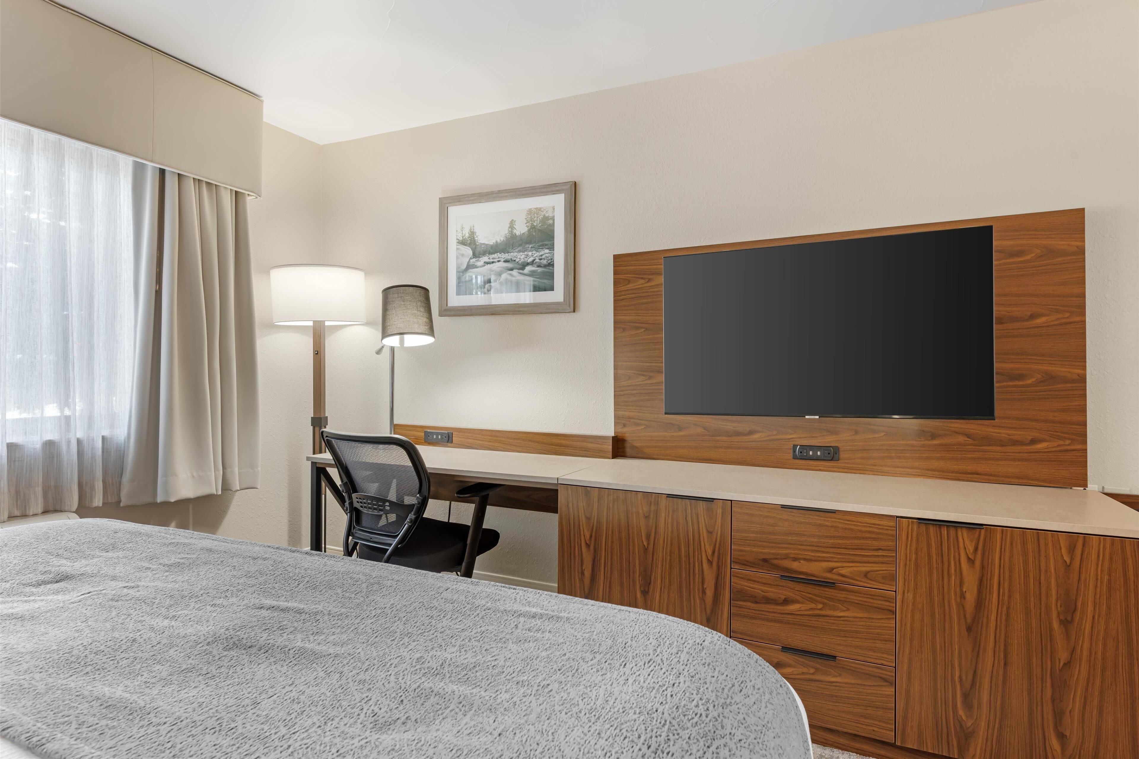 Een hotelkamer met een groot bed, een bureau met stoel, een flatscreen televisie, een lamp en een ingelijst schilderij aan de muur.