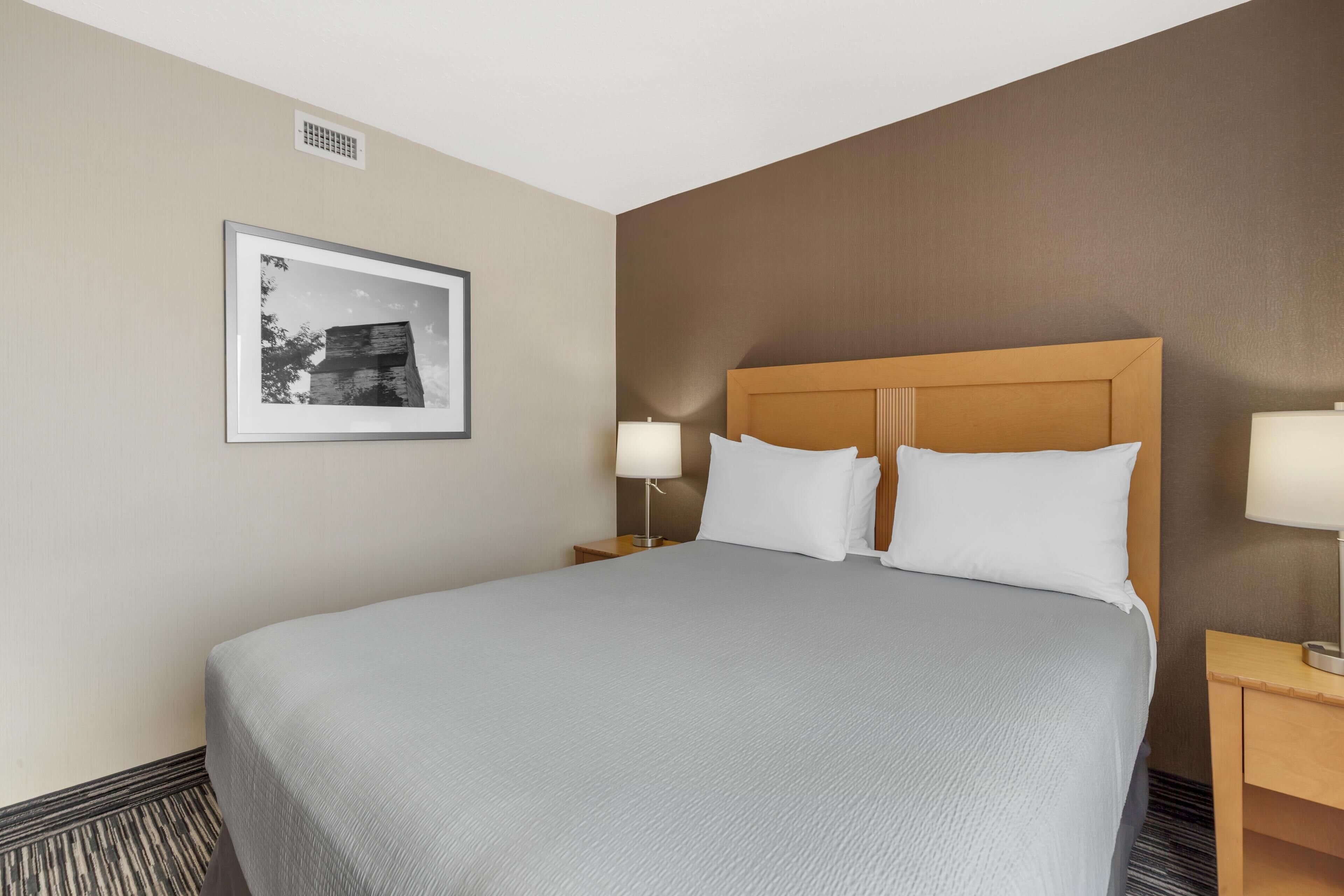 Habitación de hotel con una cama grande, dos mesitas de noche, un cuadro enmarcado en la pared y una ventana con persianas.