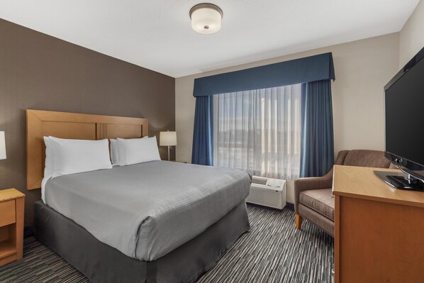 A hotel room with a large bed, a desk with a flat-screen TV, a chair, and a window with curtains. - Best Western Grande Prairie Hotel & Suites (Grande Prairie)
