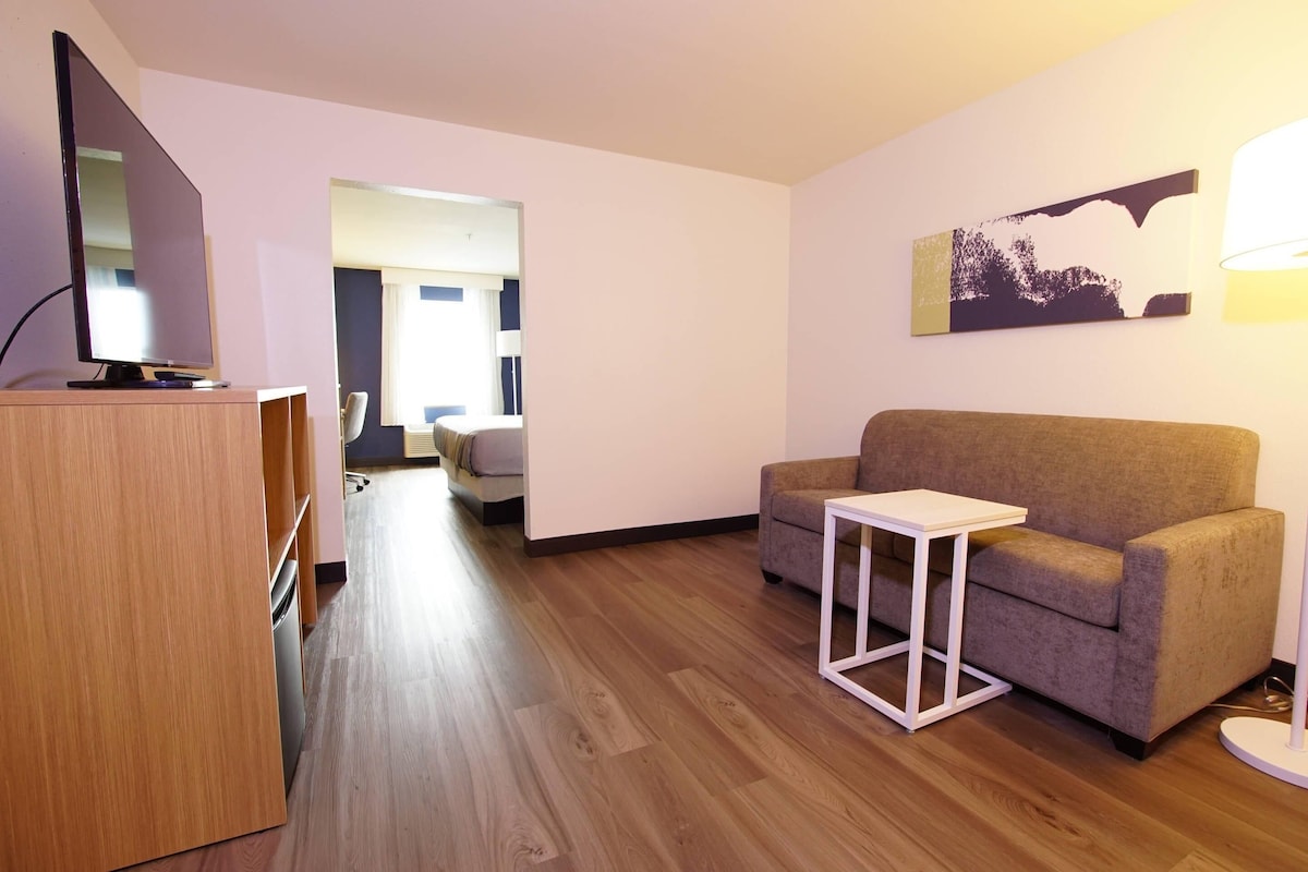 A modern living room with a flat-screen TV, a sofa, a small white table, and a lamp.