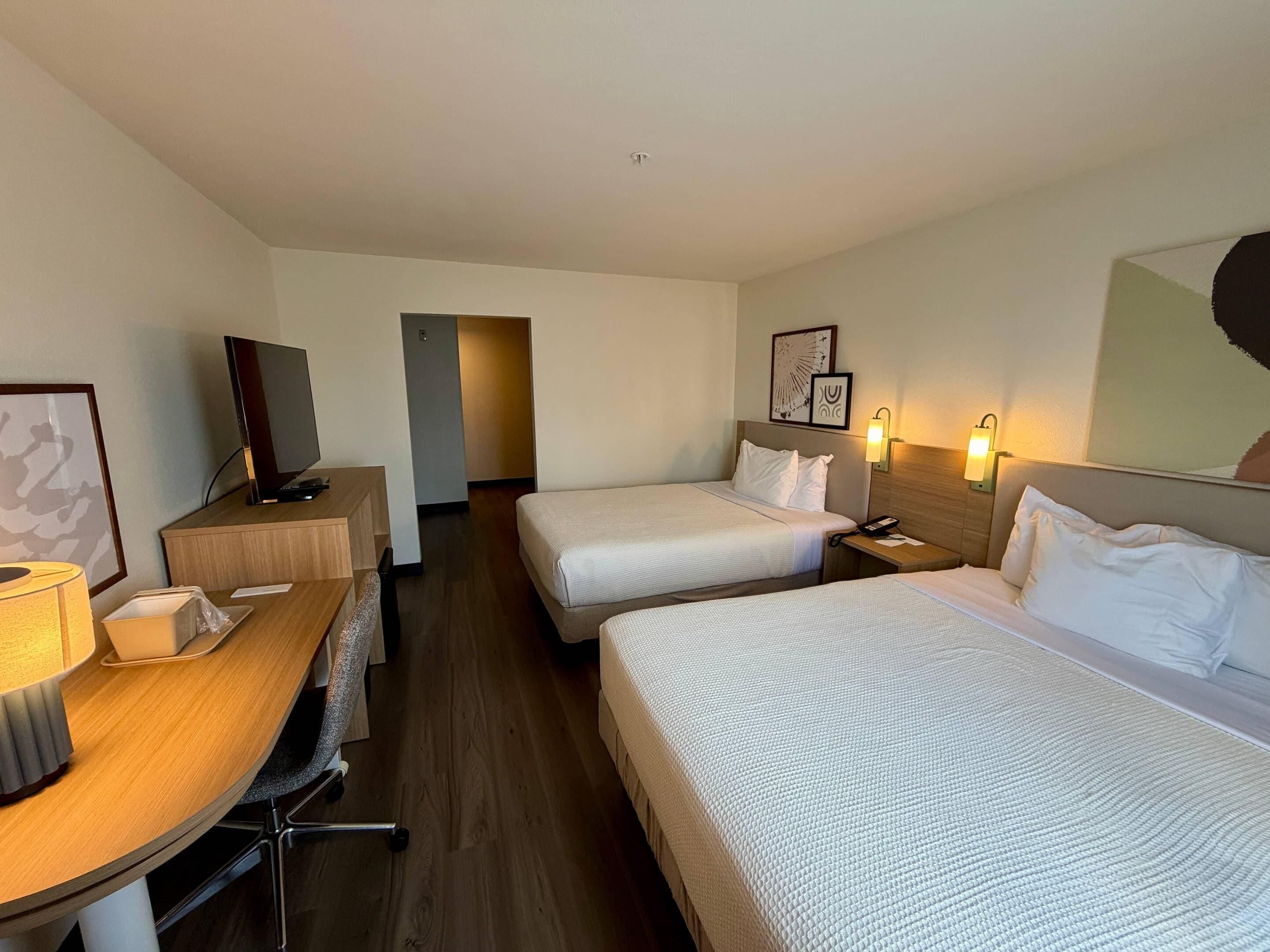 A hotel room with two beds, a desk with a chair, a television, and a lamp.