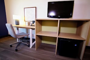 Een hotelkamer met een bureau, stoel, televisie en een klein zwart apparaat.