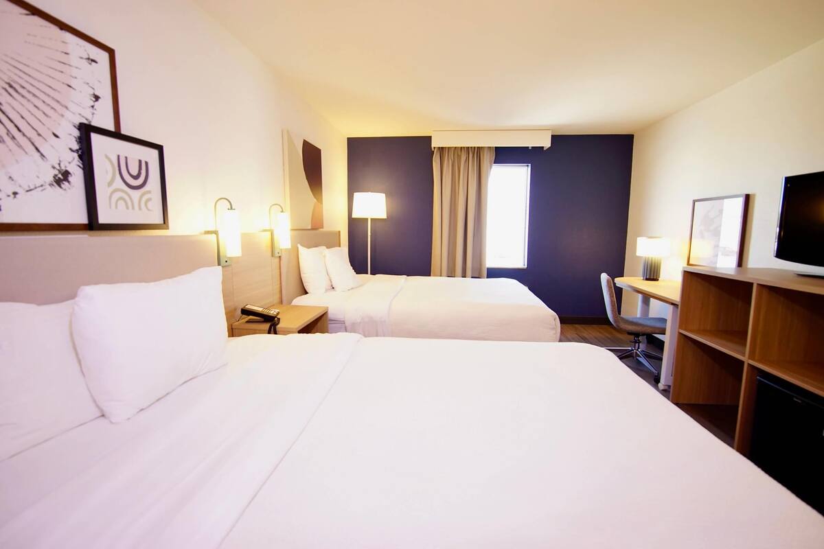 Une chambre d’hôtel avec deux lits, un bureau, une chaise, une télévision et des œuvres d’art accrochées aux murs.