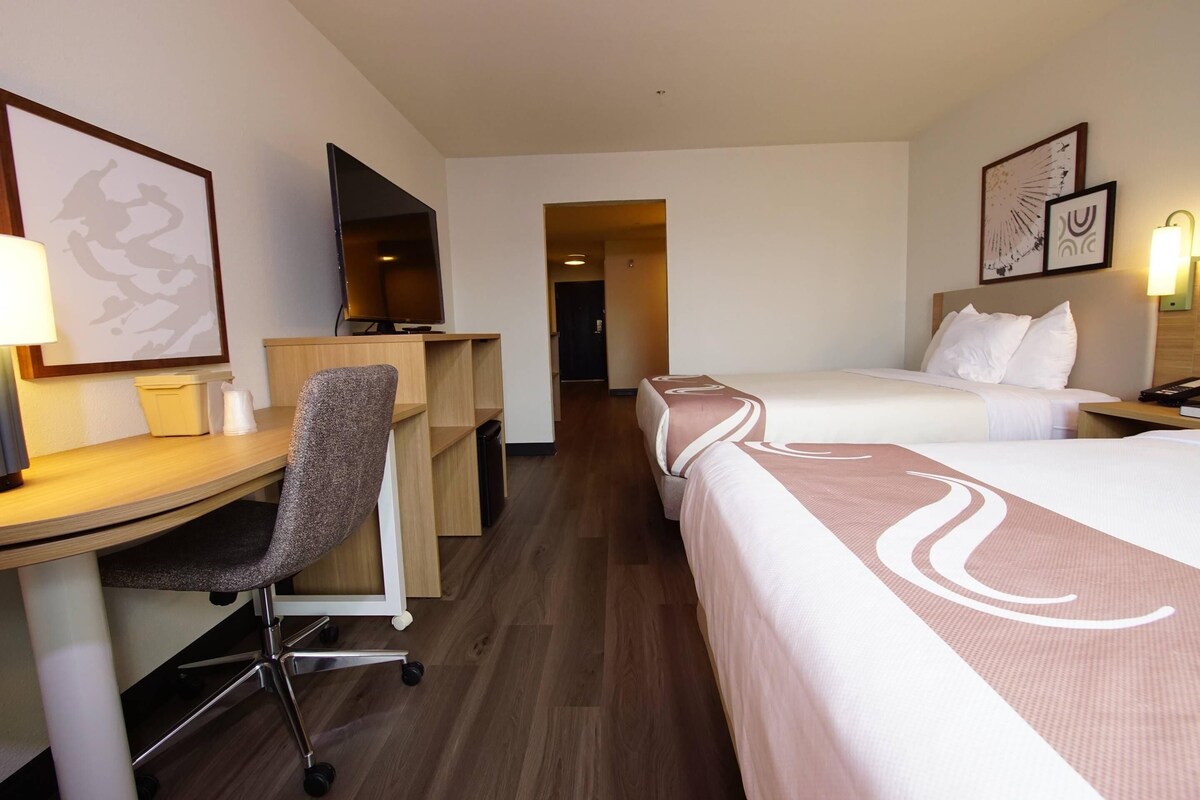 A hotel room with a desk, chair, bed, and a television.