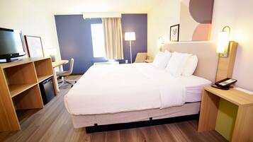 A hotel room with a bed, desk, chair, TV, and bedside table.