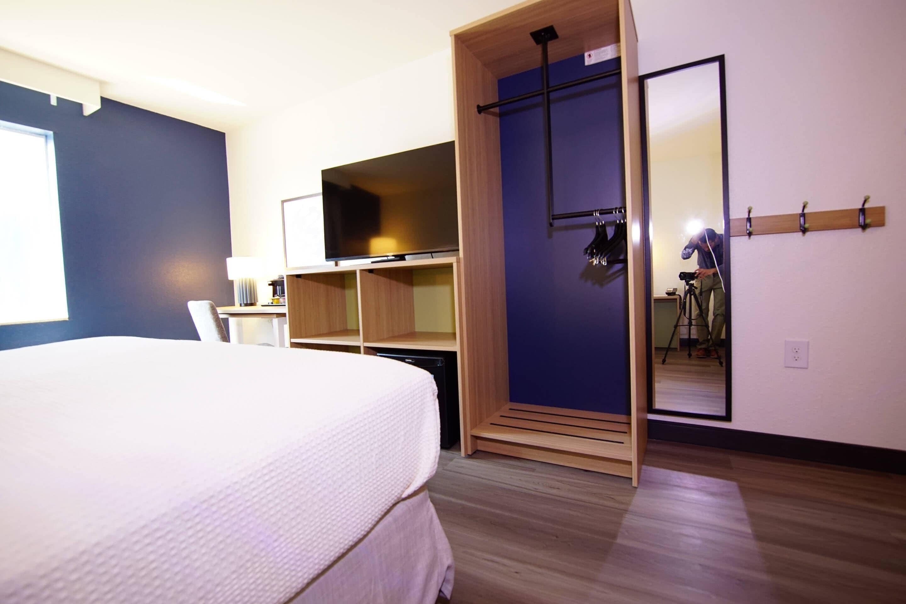 Quarto com uma cama, televisão, guarda-roupa e espelho.