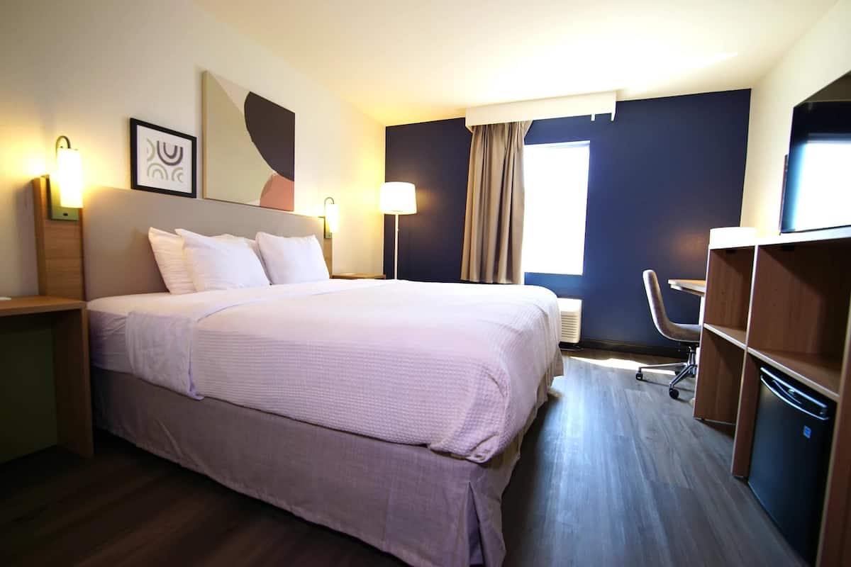 Une chambre d’hôtel comprenant un lit, des lampes de chevet, un bureau, une chaise, une armoire et une fenêtre avec des rideaux.