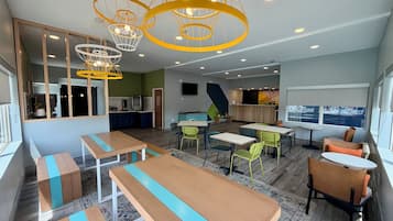 A modern interior with wooden tables and chairs, a kitchen area, and a seating area with a large window.