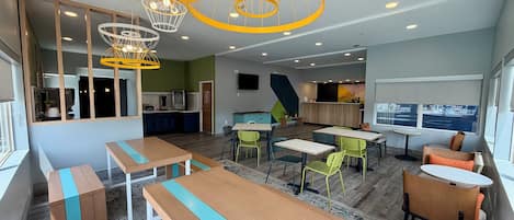 A modern interior with wooden tables and chairs, a kitchen area, and a seating area with a large window.