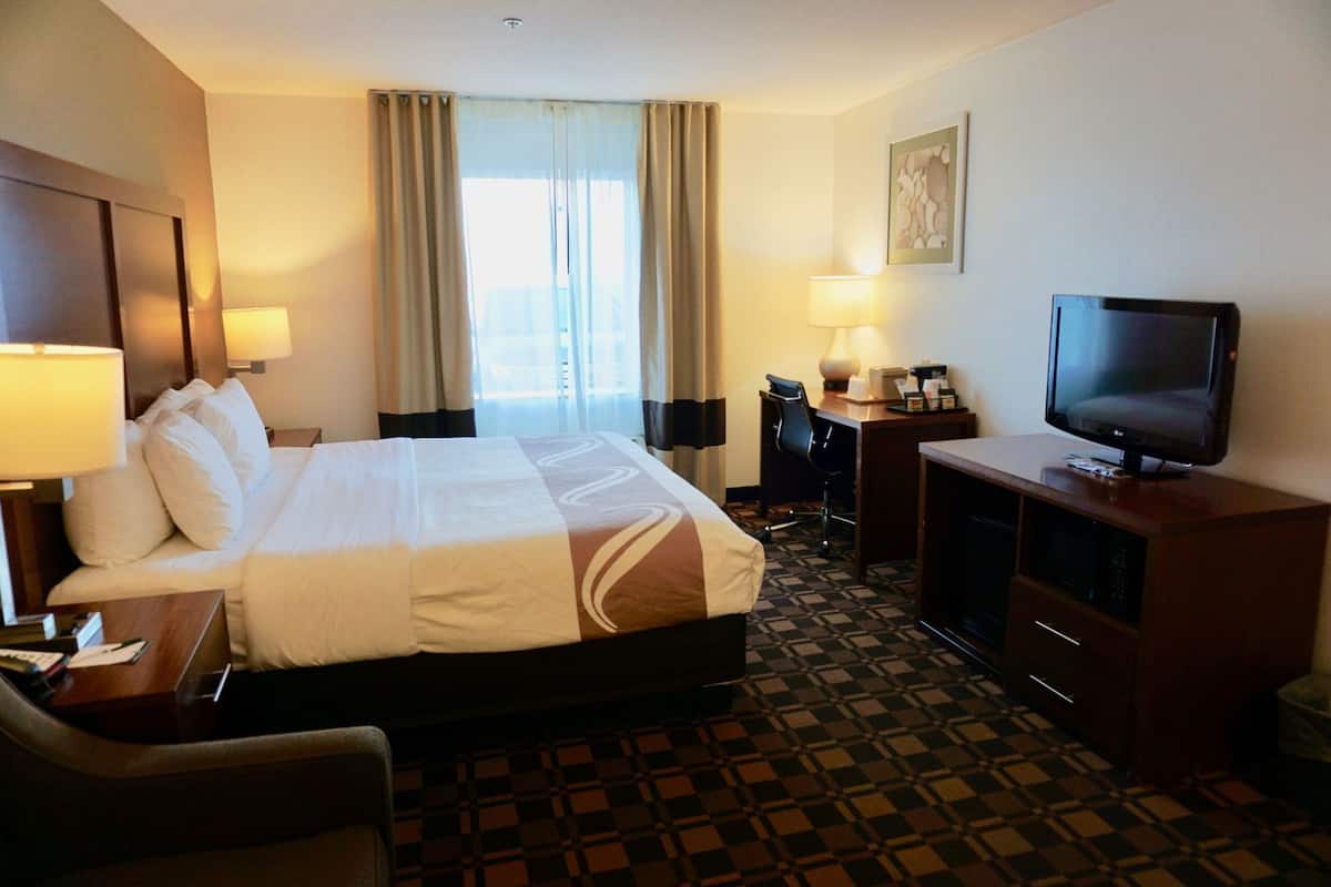 Ein Hotelzimmer mit Bett, Schreibtisch, Stuhl, Fernseher und einem Fenster mit Vorhängen.