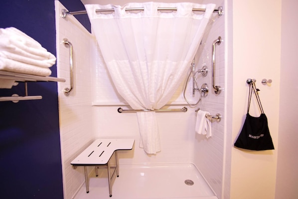 A bathroom with a shower, grab bars, a towel rack, and a small table.