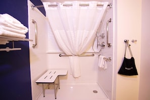 A bathroom with a shower, grab bars, a towel rack, and a small table.