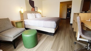 A hotel room with a bed, a desk, a chair, a green ottoman, and a wall-mounted TV. - Quality Inn & Suites Georgetown - Seaford (Georgetown)