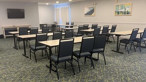 A conference room with multiple tables and chairs, a television on the wall, and two paintings.