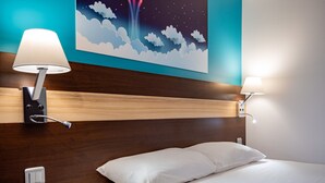 Une chambre d’hôtel avec une tête de lit en bois, deux lampes de chevet, une télécommande et une décoration murale représentant des nuages et des étoiles.