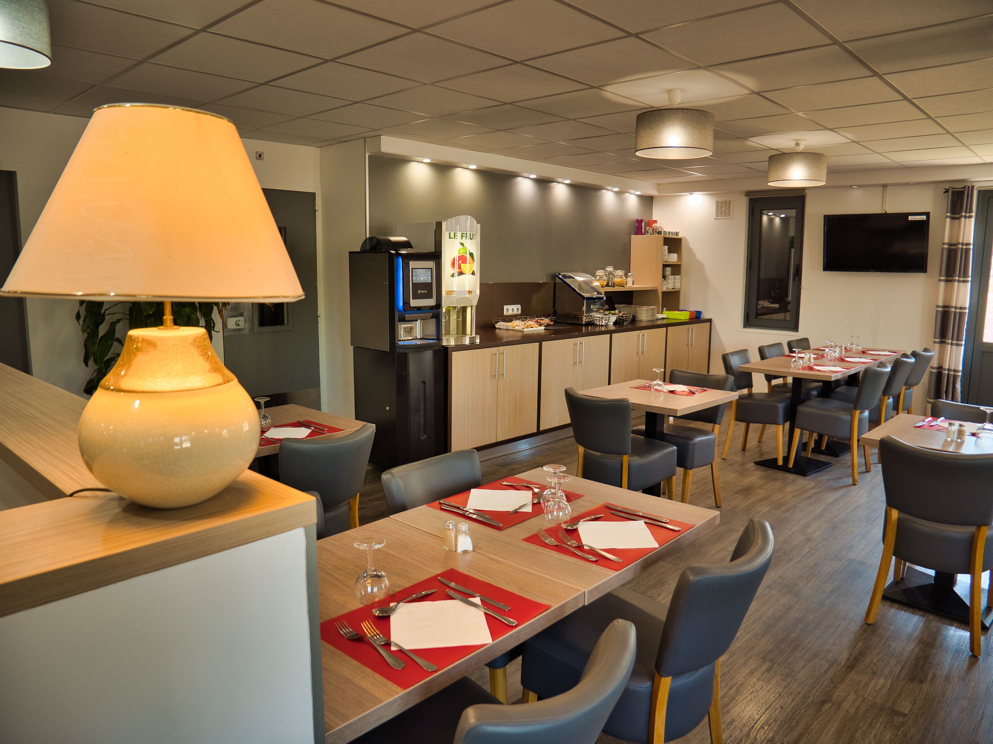 Un comedor de hotel moderno con varias mesas, sillas y una lámpara de mesa grande.