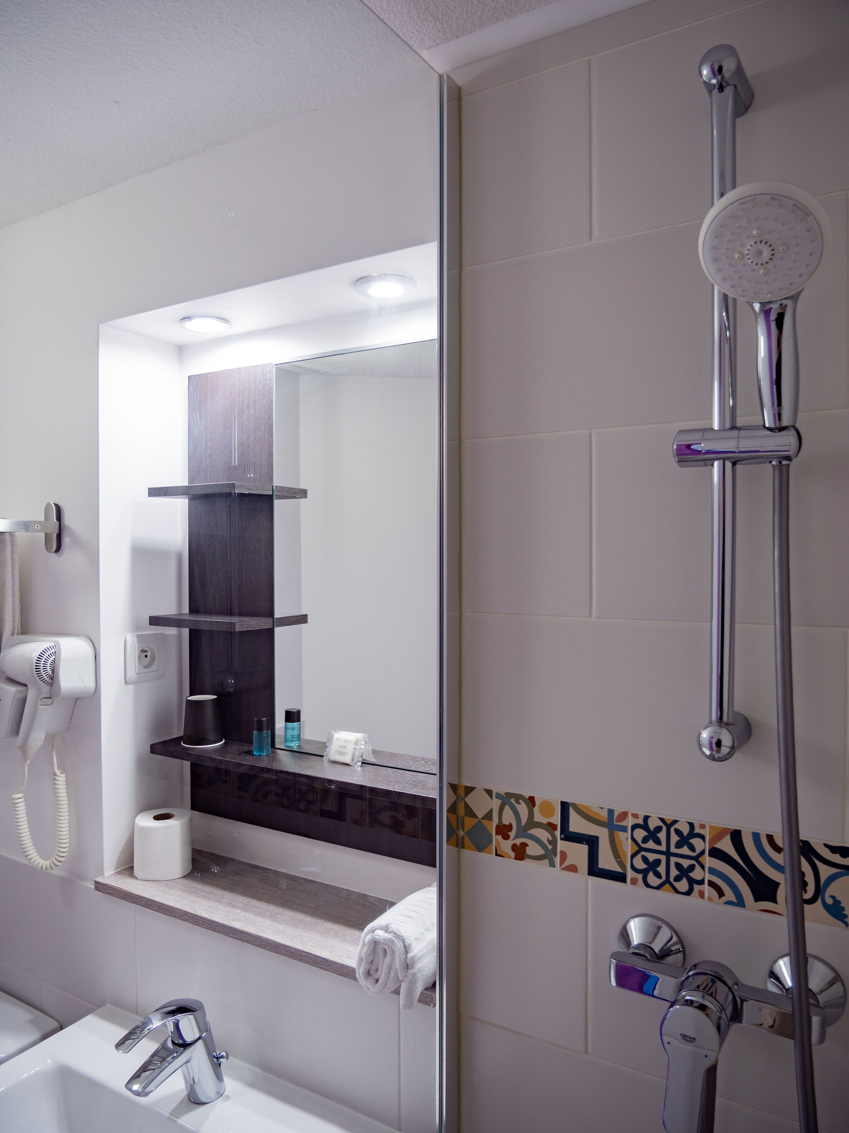 A modern bathroom with a white sink, a mirror, a hairdryer, a showerhead, and a towel rack.