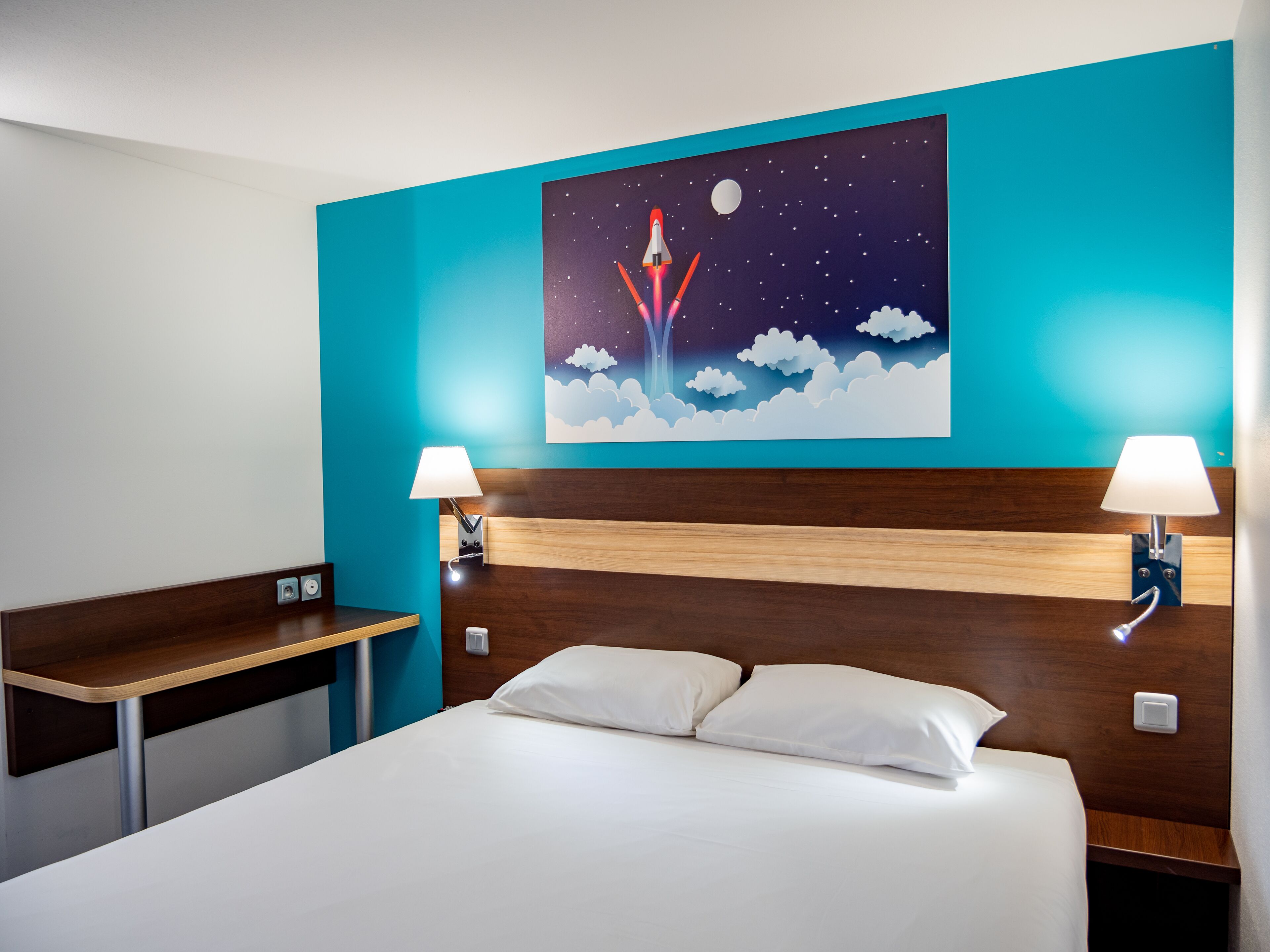 A hotel room with a bed, bedside tables, a night sky mural, and wall-mounted lamps.