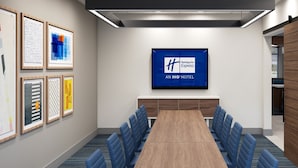 A conference room with a long table, blue chairs, framed artwork on the walls, and a large screen displaying the Holiday Inn Express logo.