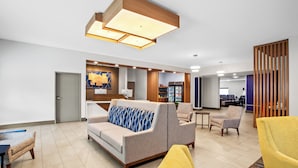 A modern hotel lobby with a sofa, armchairs, a reception desk, and a wooden partition.