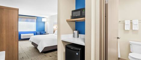 A hotel room with a bed, a microwave, a refrigerator, a sink, and a toilet.