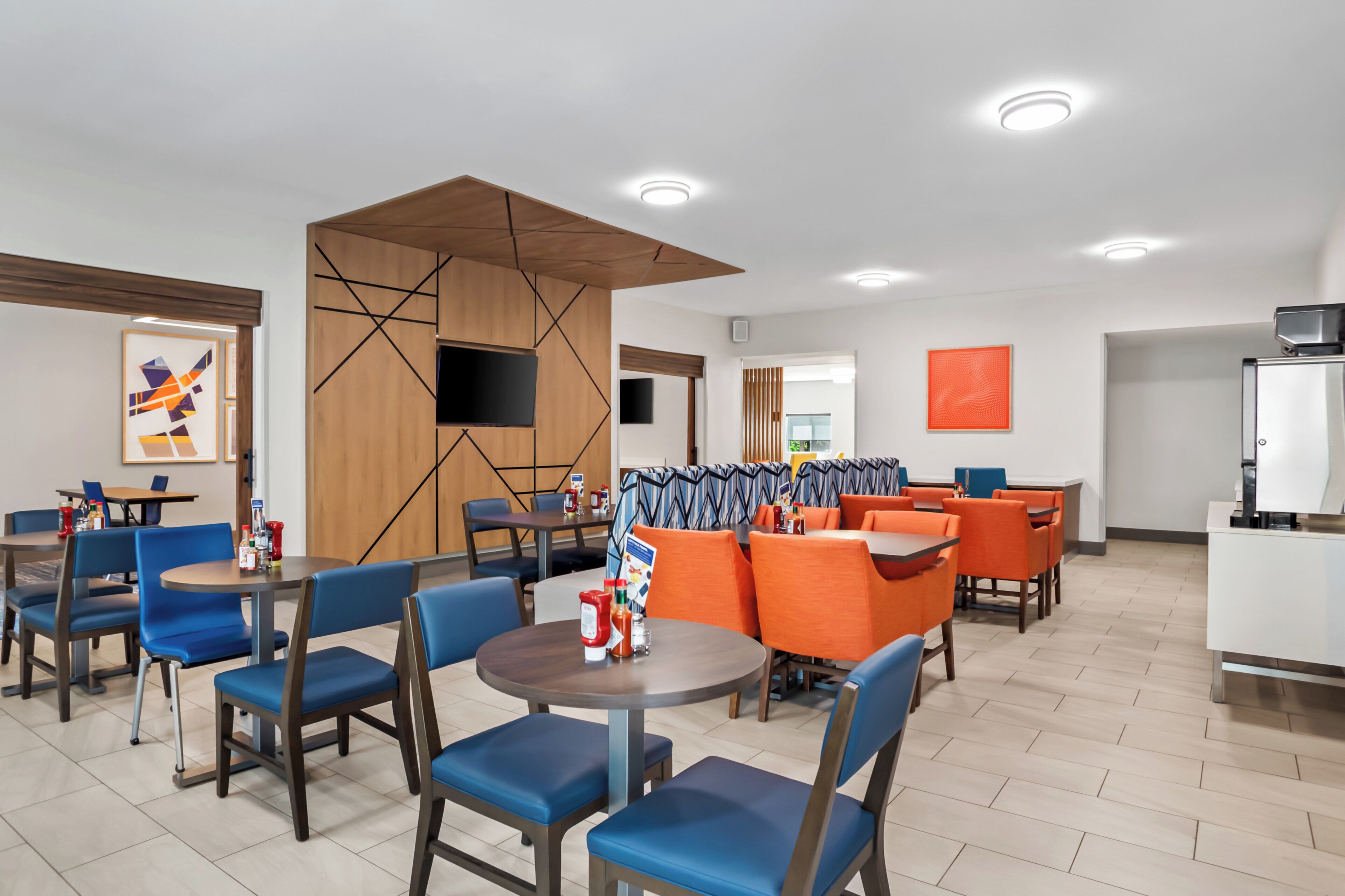 A modern dining area with blue and orange seating, a wooden partition, and a flat-screen TV mounted on the wall.